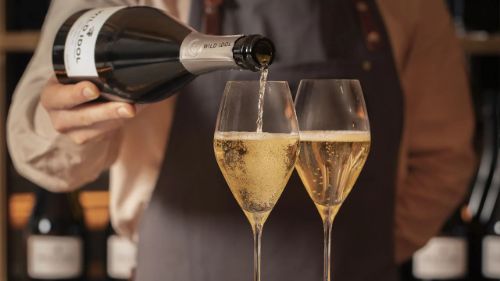 Pouring of premium non alcoholic wine into two elegant flutes, showcasing a rich, bubbly texture.