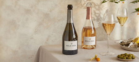 Glasses of Wild Idol Alcohol Free Sparkling Rosé and White Wine standing on a table next to their bottles