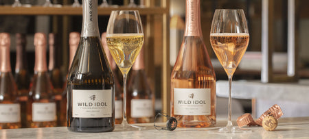 Glasses of Wild Idol Alcohol Free Sparkling Rosé & White Wine, standing on a bar next to their bottles