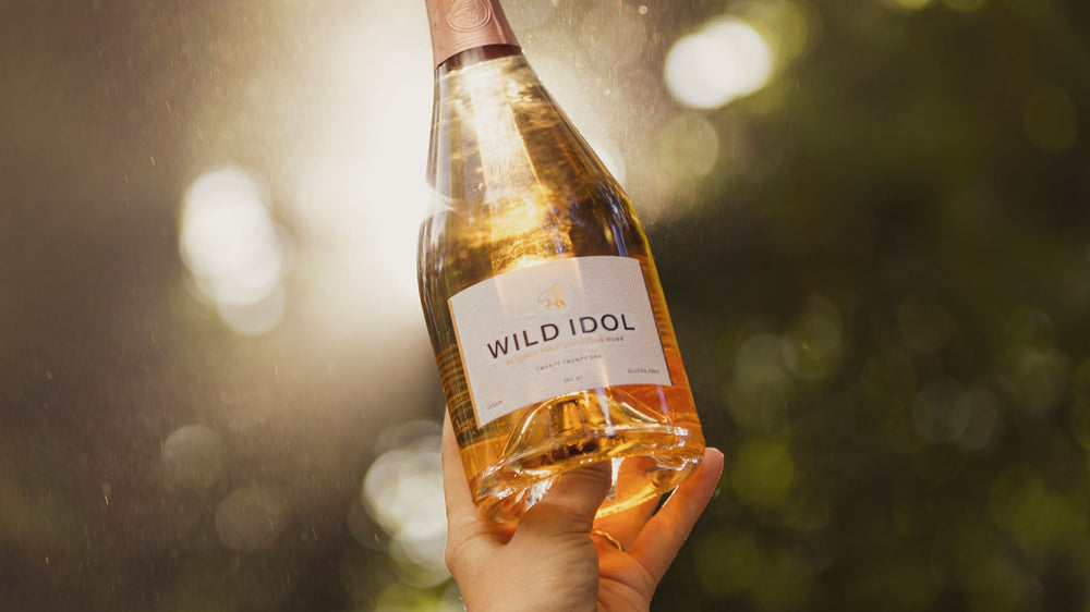 A bottle of WILD IDOL Alcohol Free Sparkling Rosé Wine being held to the sky.