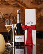 A glass and bottle of Wild Idol Alcohol Free Sparkling White Wine next to its box