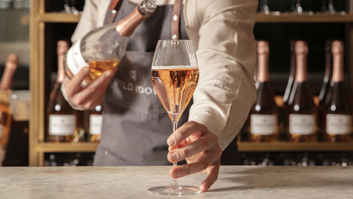 A glasses of Wild Idol Alcohol Free Sparkling Rosé being placed on a bar counter